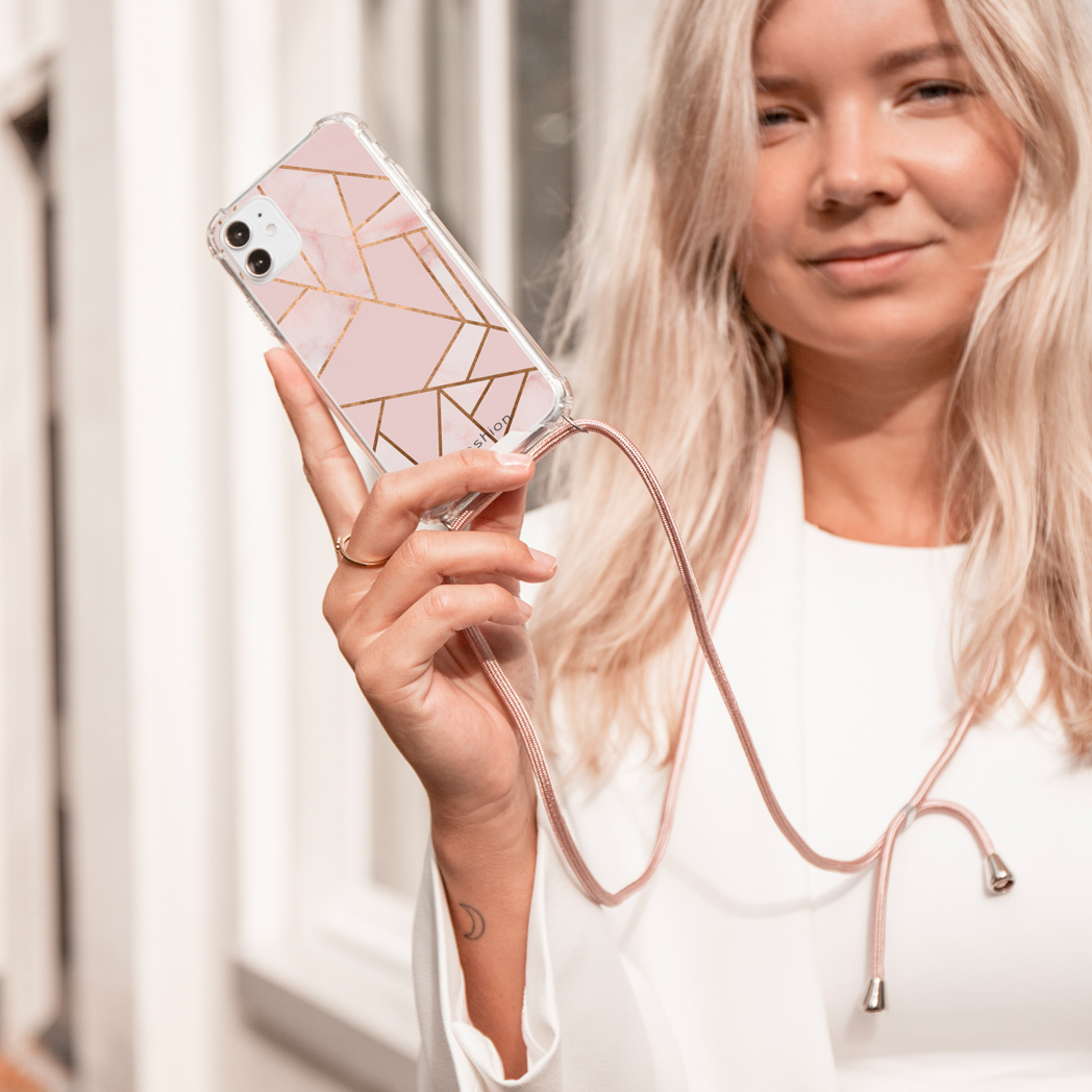 Vrouw houdt telefoon vast in een doorzichtige hoes met roze en gouden geometrisch ontwerp, aan een bandje.