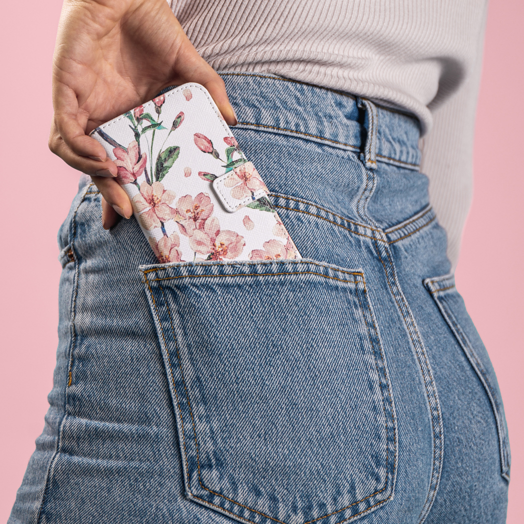 Une personne tient un téléphone dans un étui floral blanc dans sa poche arrière de jean.