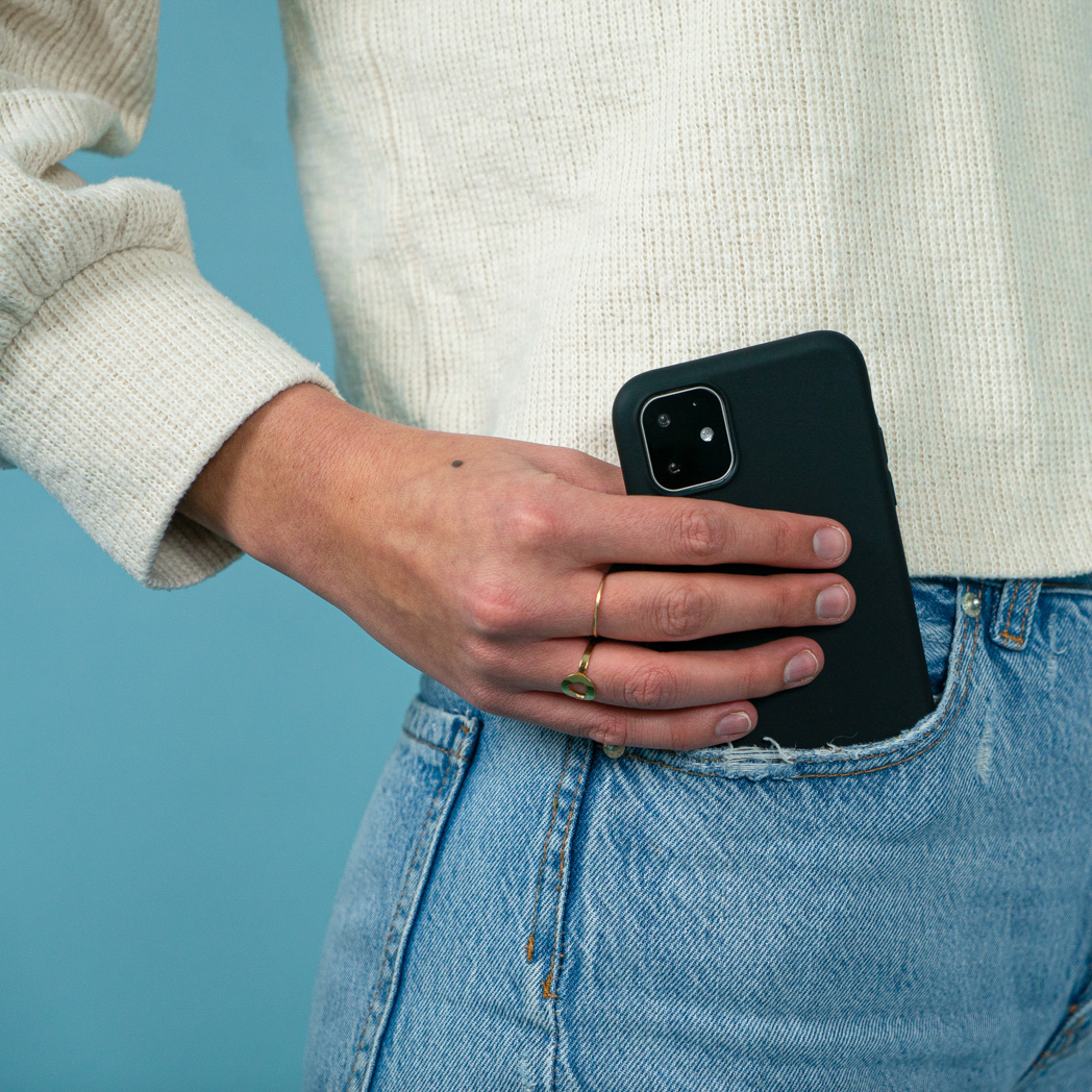 Een hand die een telefoon in een donkergroene hoes in een spijkerbroekzak houdt.