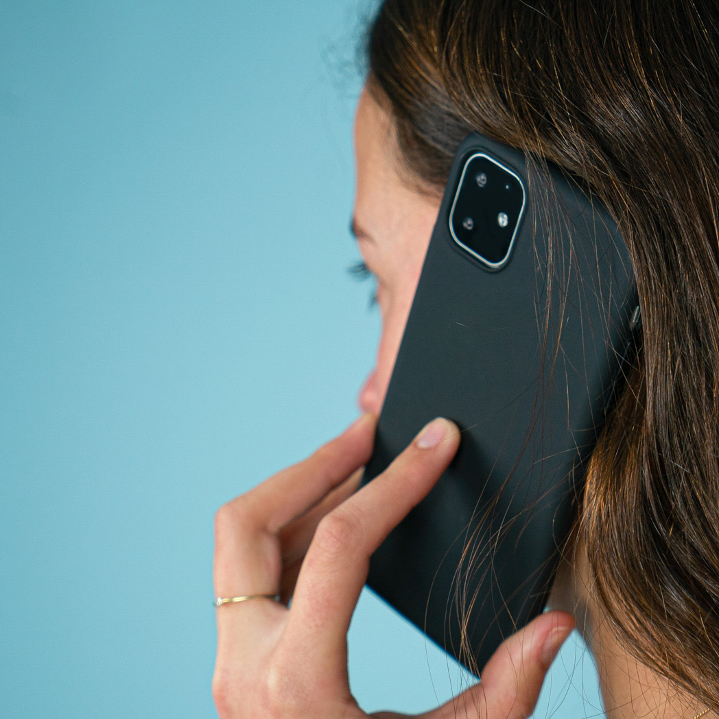 Een vrouw die een telefoon tegen haar oor houdt. Ze kijkt weg, met een blauwe achtergrond.
