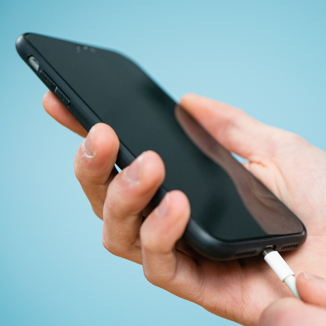 Hand die een telefoon vasthoudt met een kabel erin.