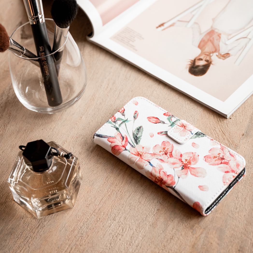 Un étui de téléphone floral, du parfum et des pinceaux de maquillage sur une table. Un magazine ouvert en arrière-plan.