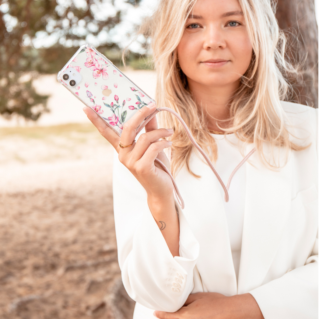 Blonde vrouw die een bloemen telefoonhoesje vasthoudt met een roze bandje.