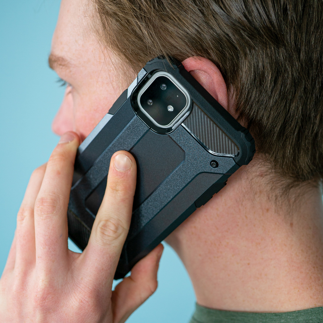 Een man houdt een zwarte telefoon in een zwarte hoes tegen zijn oor. De achtergrond is blauw.