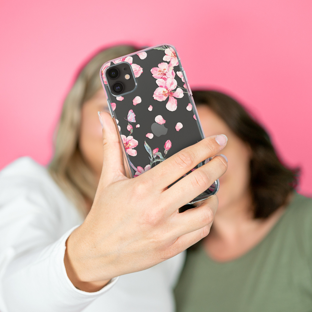 Deux femmes prenant un selfie avec un téléphone dans un étui fleuri, sur un fond rose.