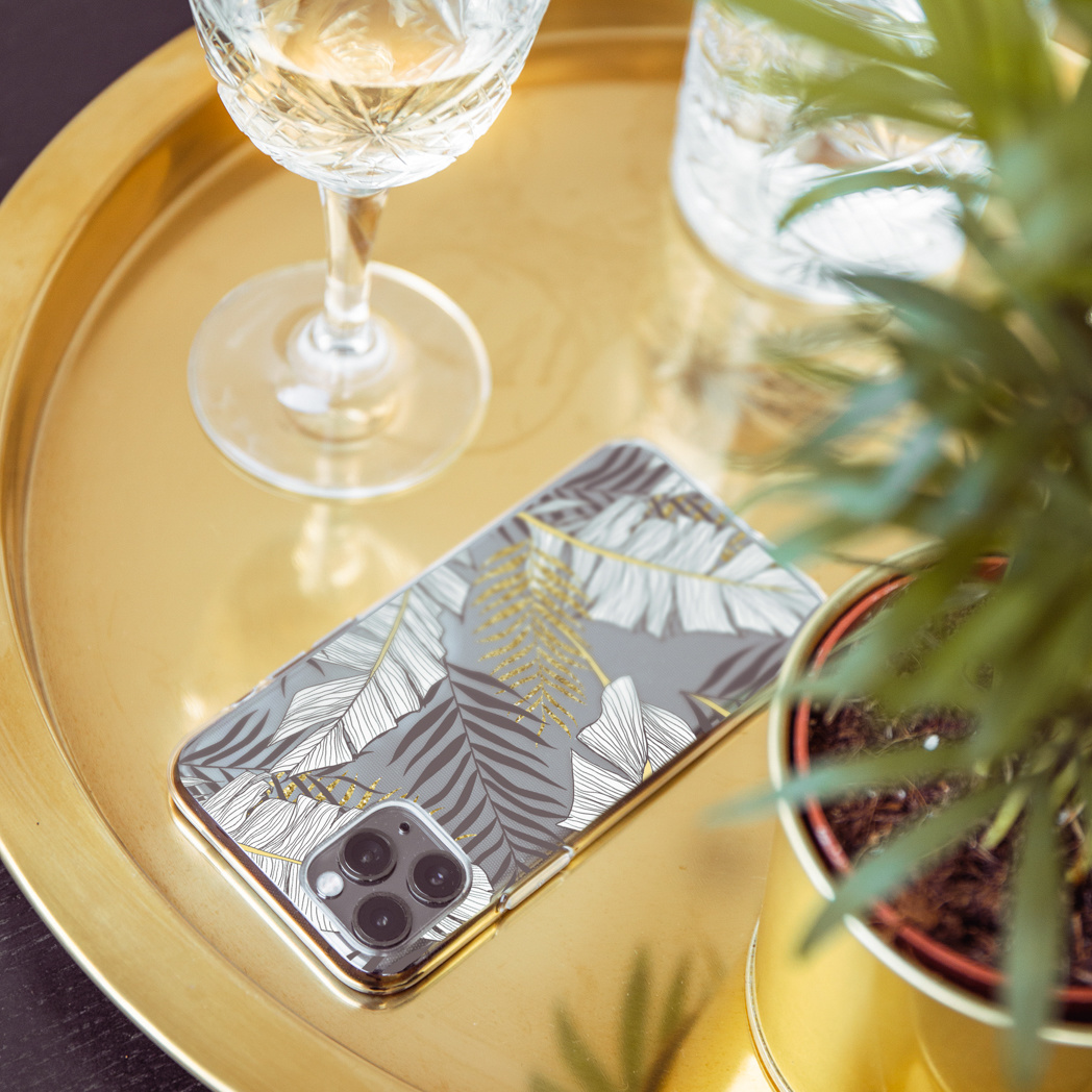 Telefoonhoesje met een bladpatroon, liggend op een dienblad met een glas en een plant.