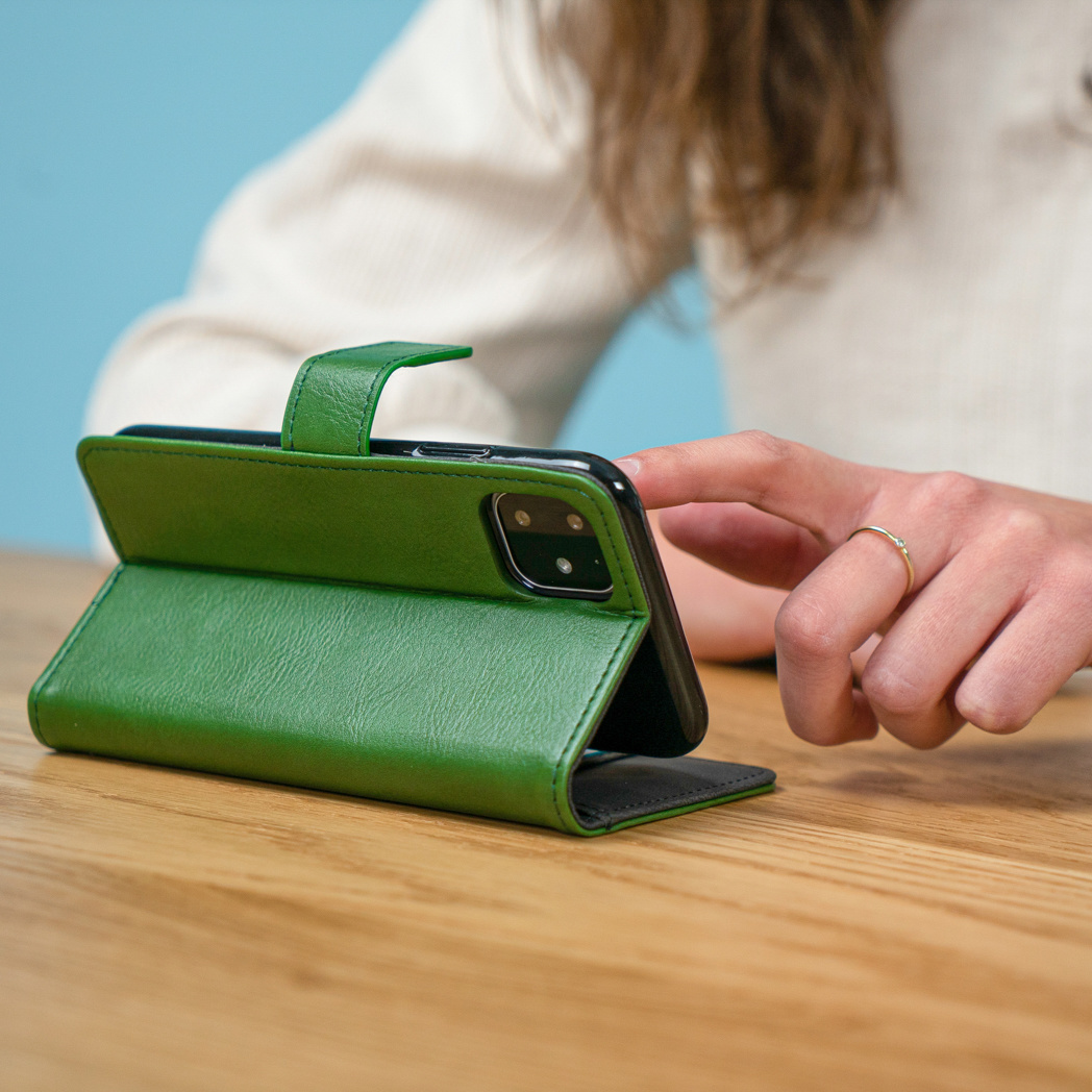 Een persoon die een groene leren telefoonhoes gebruikt met een telefoon op een houten tafel.