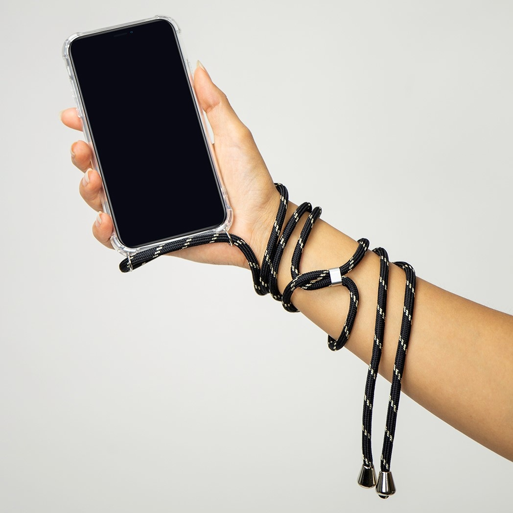 Une main tenant un téléphone avec une coque transparente, attachée à un cordon noir et doré.
