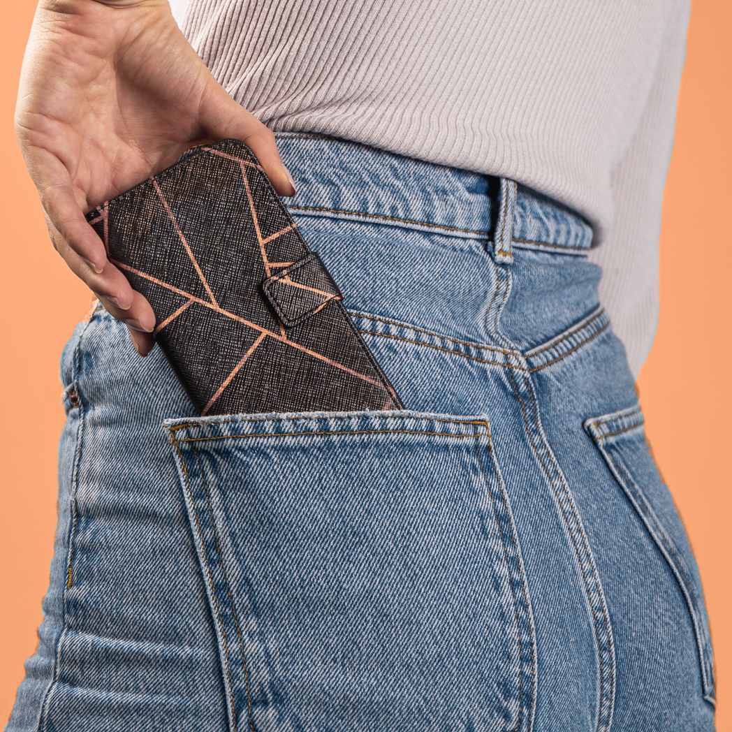 Hand steekt een telefoon in een jeanszak. De telefoon heeft een oranje patroon.