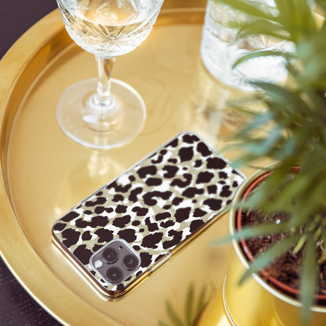 Un étui de téléphone avec un imprimé léopard sur un plateau doré, avec un verre à vin et une plante en arrière-plan.
