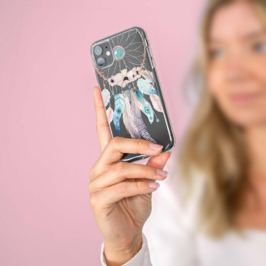 Die Hand einer Frau hält eine Handyhülle mit einem Traumfänger-Design. Der Hintergrund ist rosa.