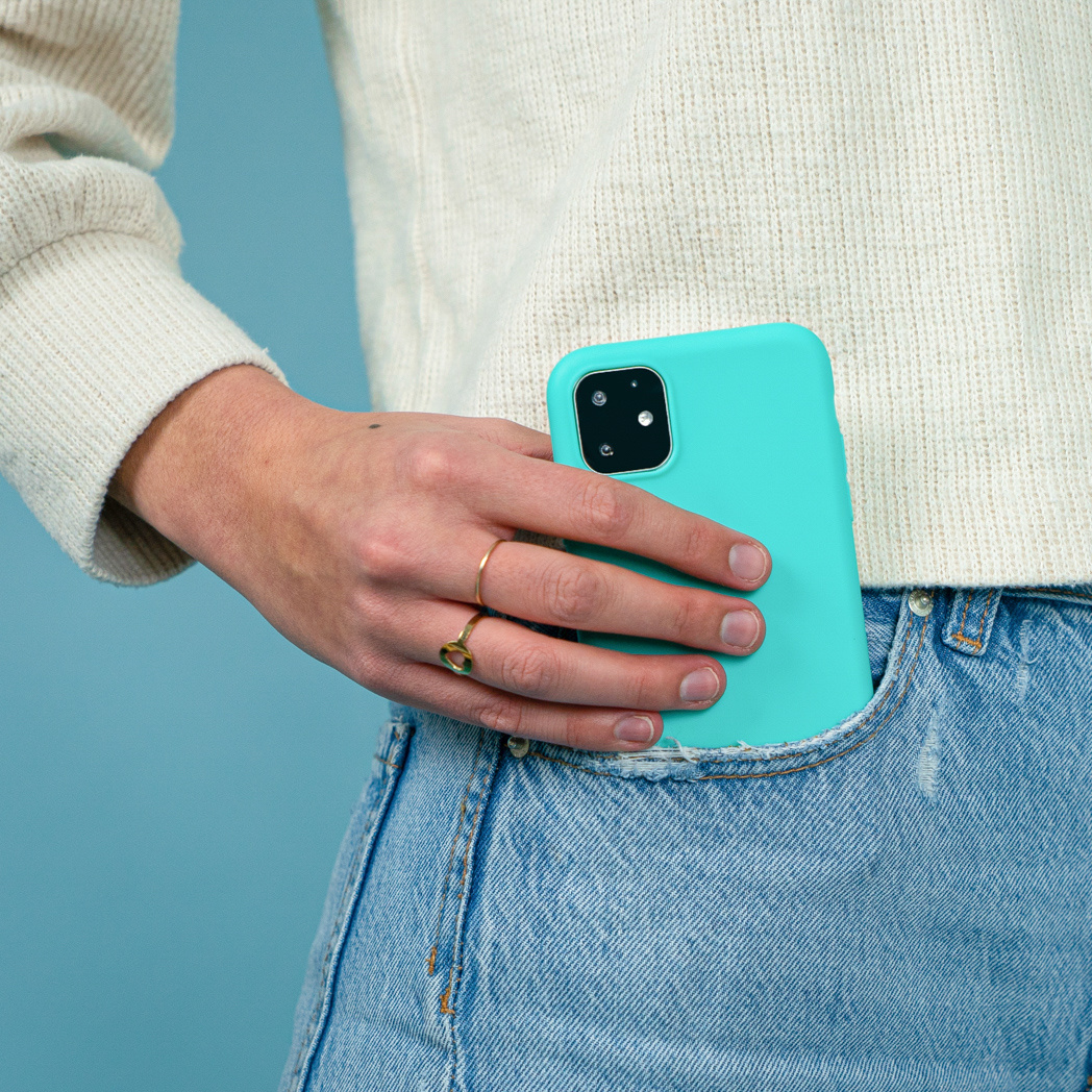 De hand van een persoon die een telefoon in een teal hoesje in een jeanszak houdt.