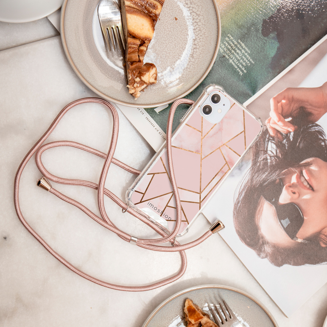 Telefoonhoesje met roze marmer en goud geometrisch ontwerp, liggend op tijdschrift en bord met cake.