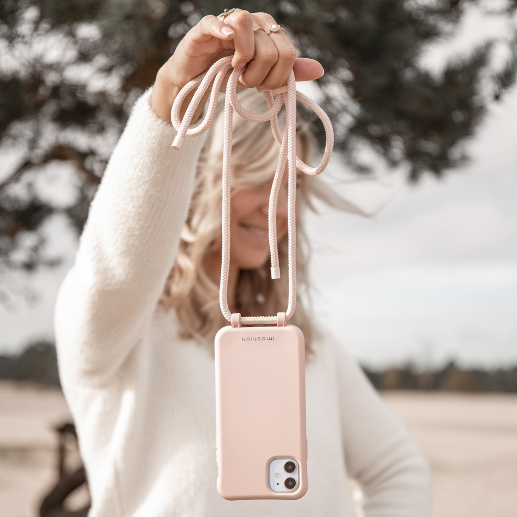 Een vrouw die een roze telefoonhoesje met een koord vasthoudt. De achtergrond is een vage buitenscène.