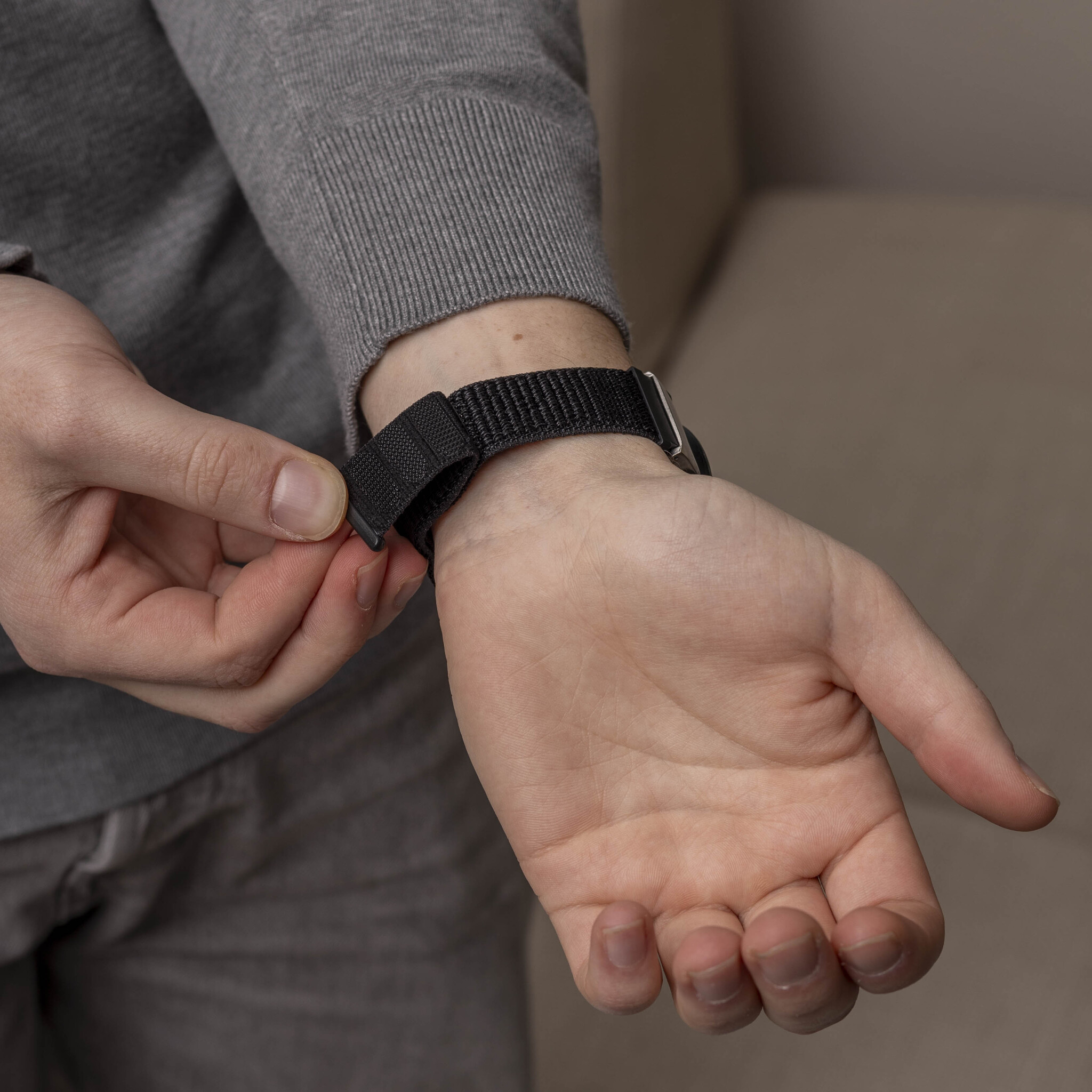 Die Hand einer Person, mit einem schwarzen Uhrenarmband, die die Uhr am Handgelenk befestigt.