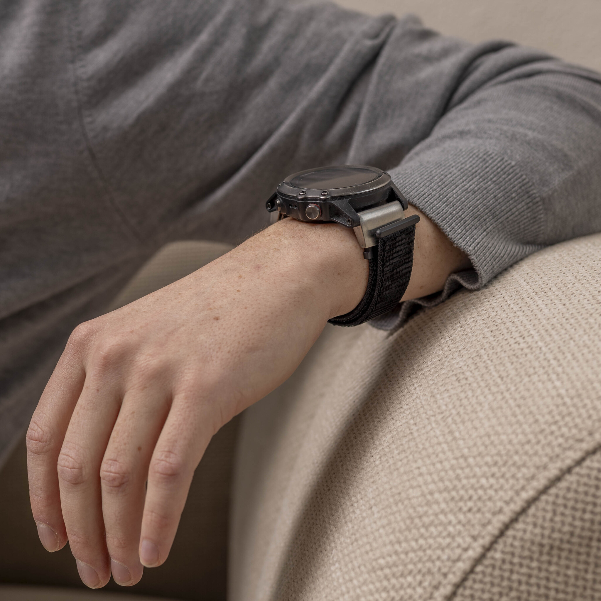 Der Arm einer Person mit einer Uhr daran, der auf einer Couch ruht.