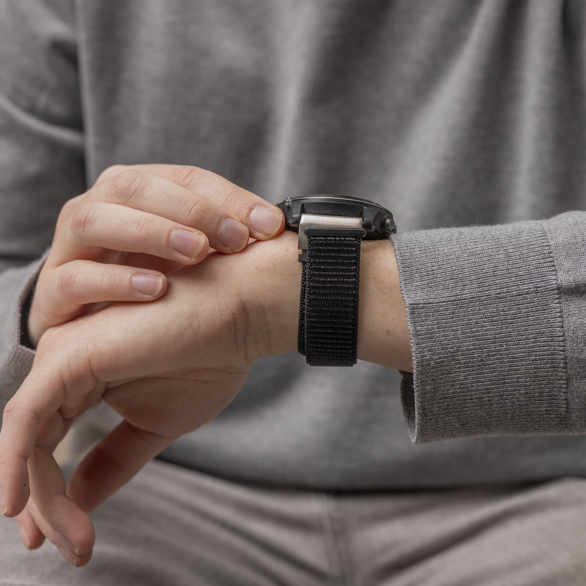 Das Handgelenk einer Person mit einer schwarzen Uhr und einem schwarzen Armband.