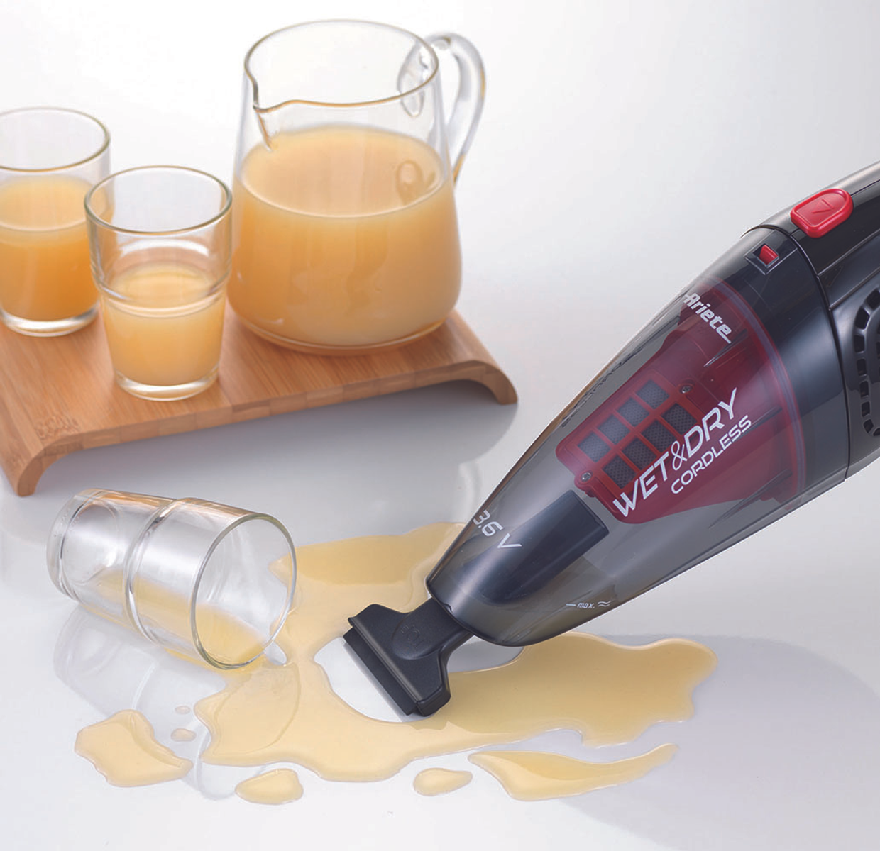 A hand vacuum is cleaning spilled juice. Two glasses and a pitcher of juice are on the table.
