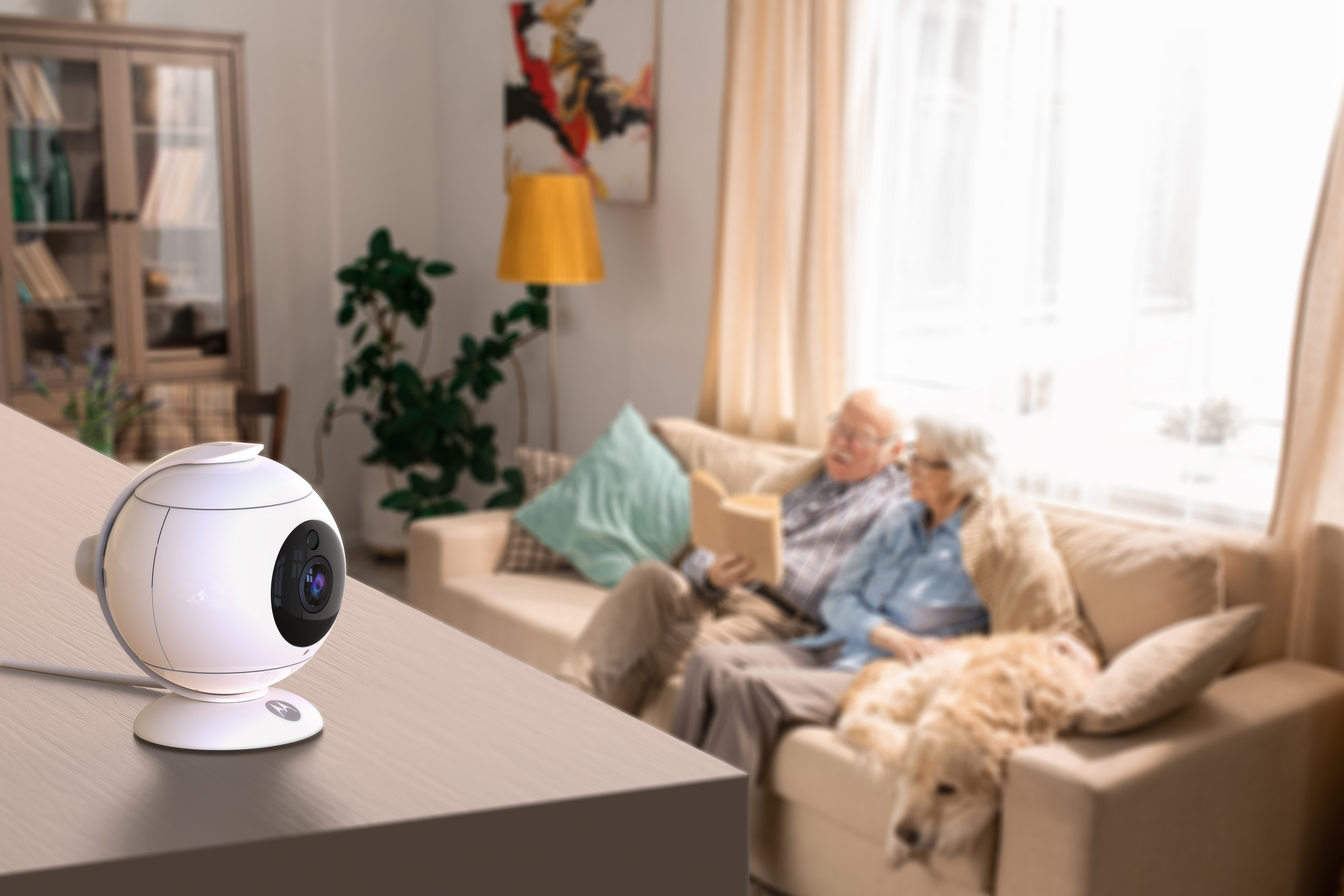 White security camera on table. Elderly couple on couch in background.