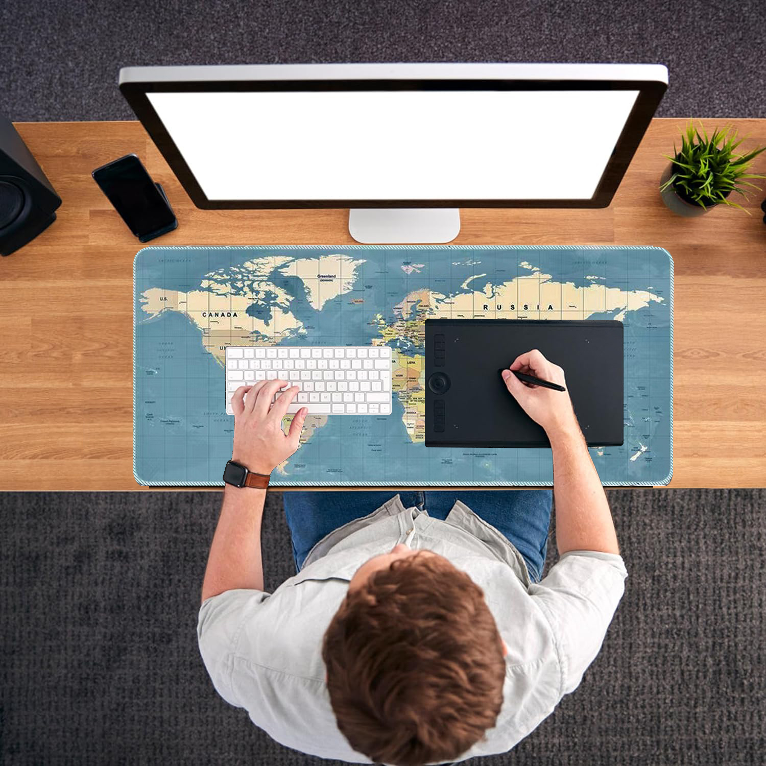 Vue aérienne d'un homme travaillant à un bureau avec un ordinateur et une tablette graphique, tapis de souris carte du monde.