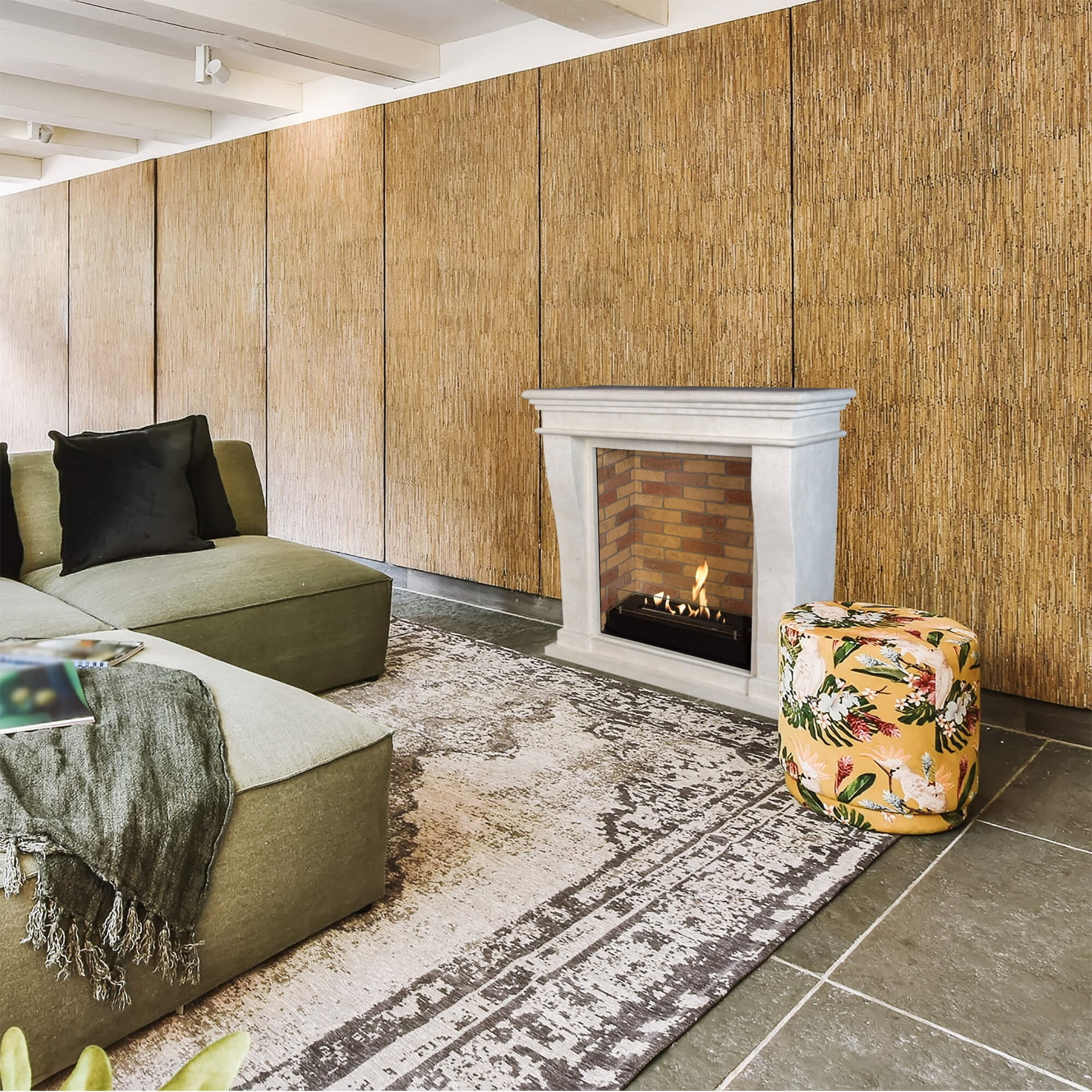 Woonkamer met groene bank, open haard, bloemenpoef en patroonkleed.