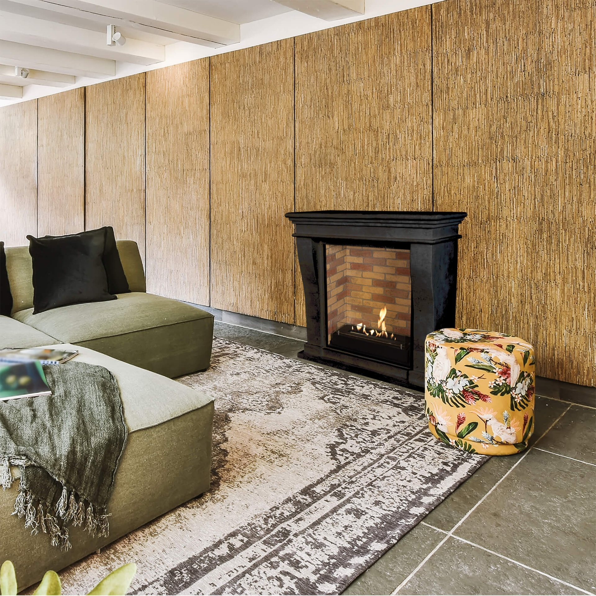 Woonkamer met olijfgroene bank, open haard, bloemenpoef en vloerkleed. Houten wand achtergrond.