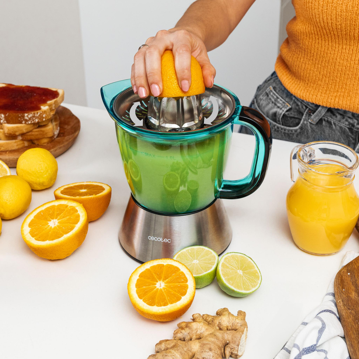 Una persona exprimiendo una naranja con un exprimidor. Naranjas, limones y jengibre en rodajas en la mesa.