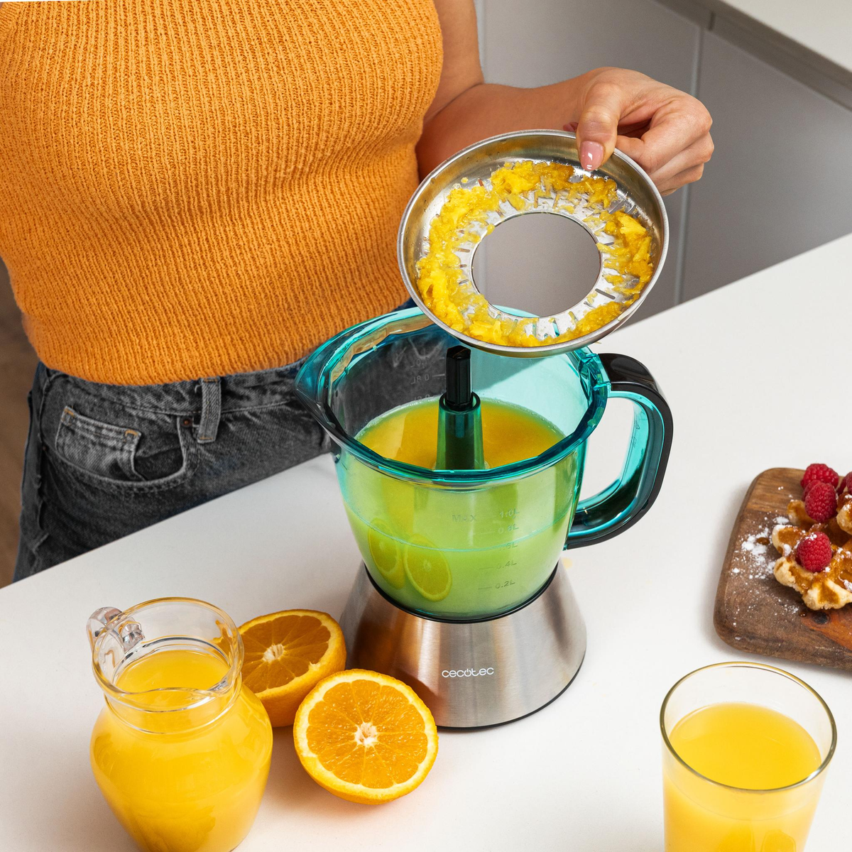 Una persona exprimiendo naranjas. Se ve una exprimidora, naranjas y jugo.