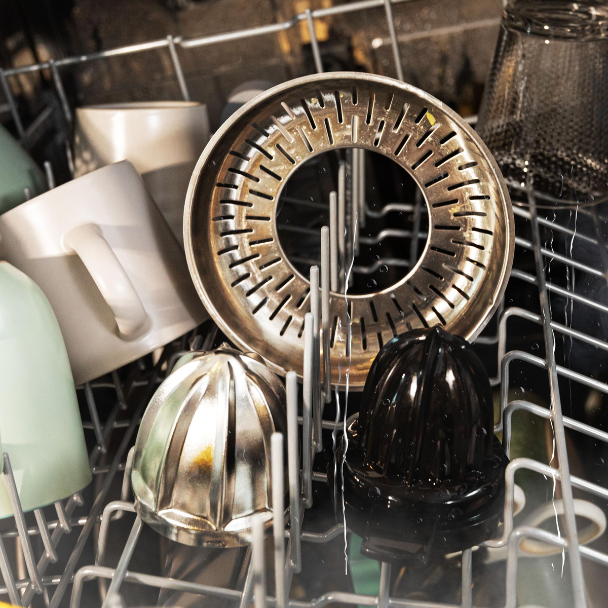 Interior de lavavajillas con varios elementos: tazas, un exprimidor y otros objetos.