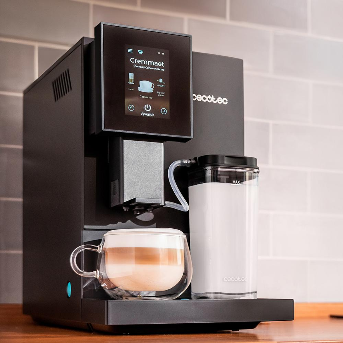 Macchina da caffè nera, con una tazza di latte e una caraffa per il latte. Sfondo grigio chiaro.