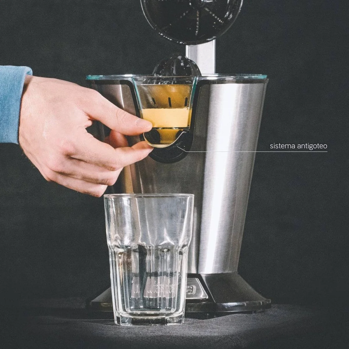 Una mano versa succo in un bicchiere da uno spremiagrumi in acciaio inossidabile, su sfondo nero.