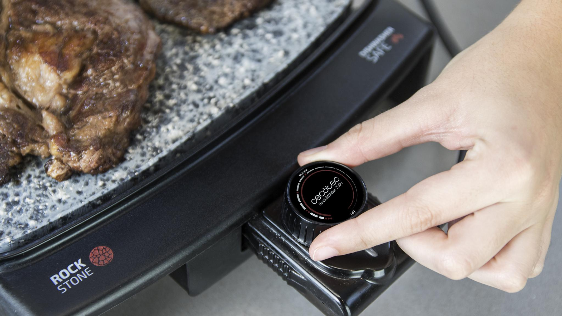 Ręka obraca czarne pokrętło na grillu Rock Stone, mięso się smaży na powierzchni.