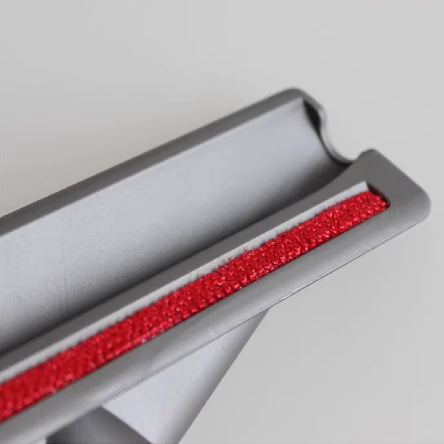 Zbliżenie szarej głowicy szczotki do odkurzacza z czerwonym, teksturowanym paskiem pośrodku.