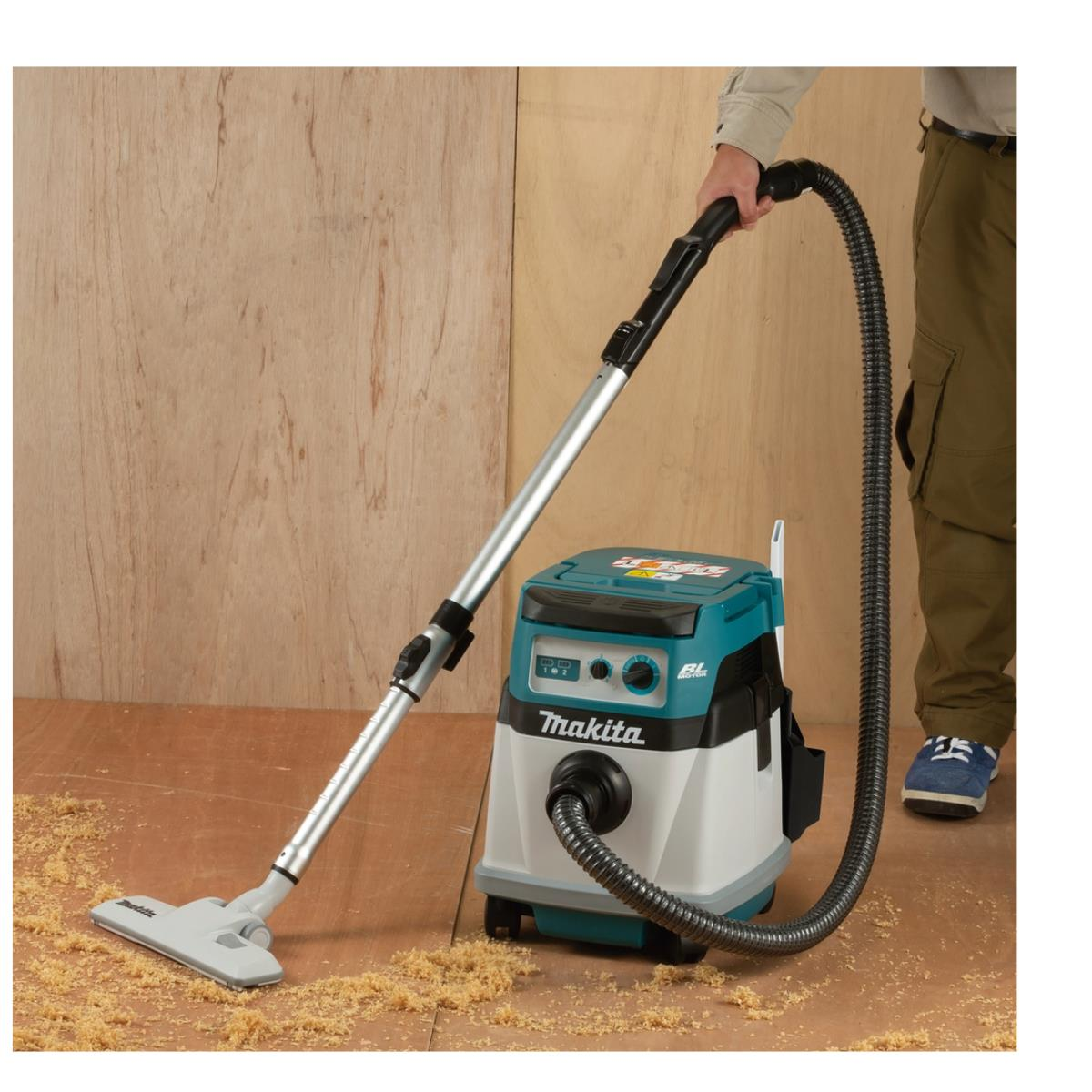 Una persona aspira segatura su un pavimento in legno con un aspirapolvere Makita.