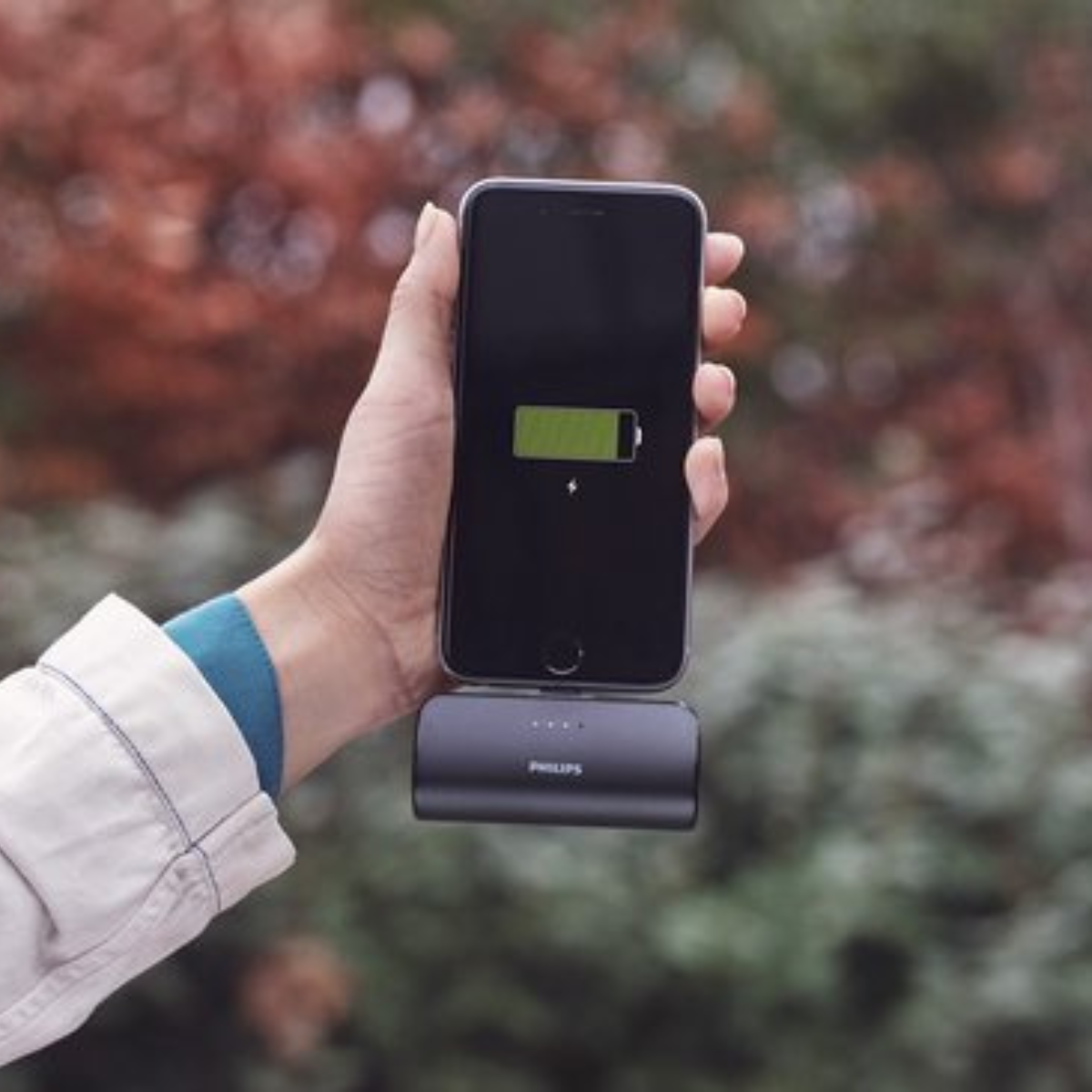 Une main tenant un téléphone en charge sur un chargeur sans fil, avec une icône de batterie verte.