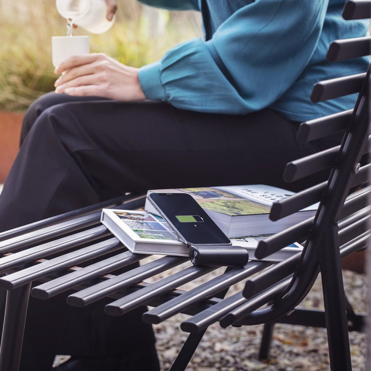 Une personne assise sur un banc avec un téléphone en charge et un livre. Ils versent de l'eau.