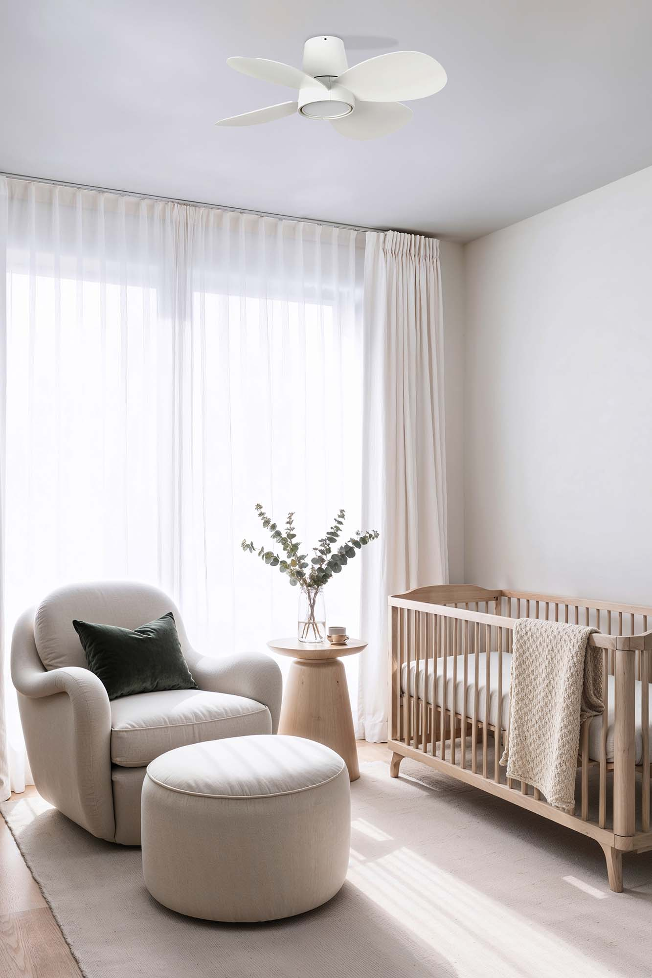 Helles Kinderzimmer mit weißen Wänden, einem Kinderbett, einem Stuhl und einem kleinen Deckenventilator.