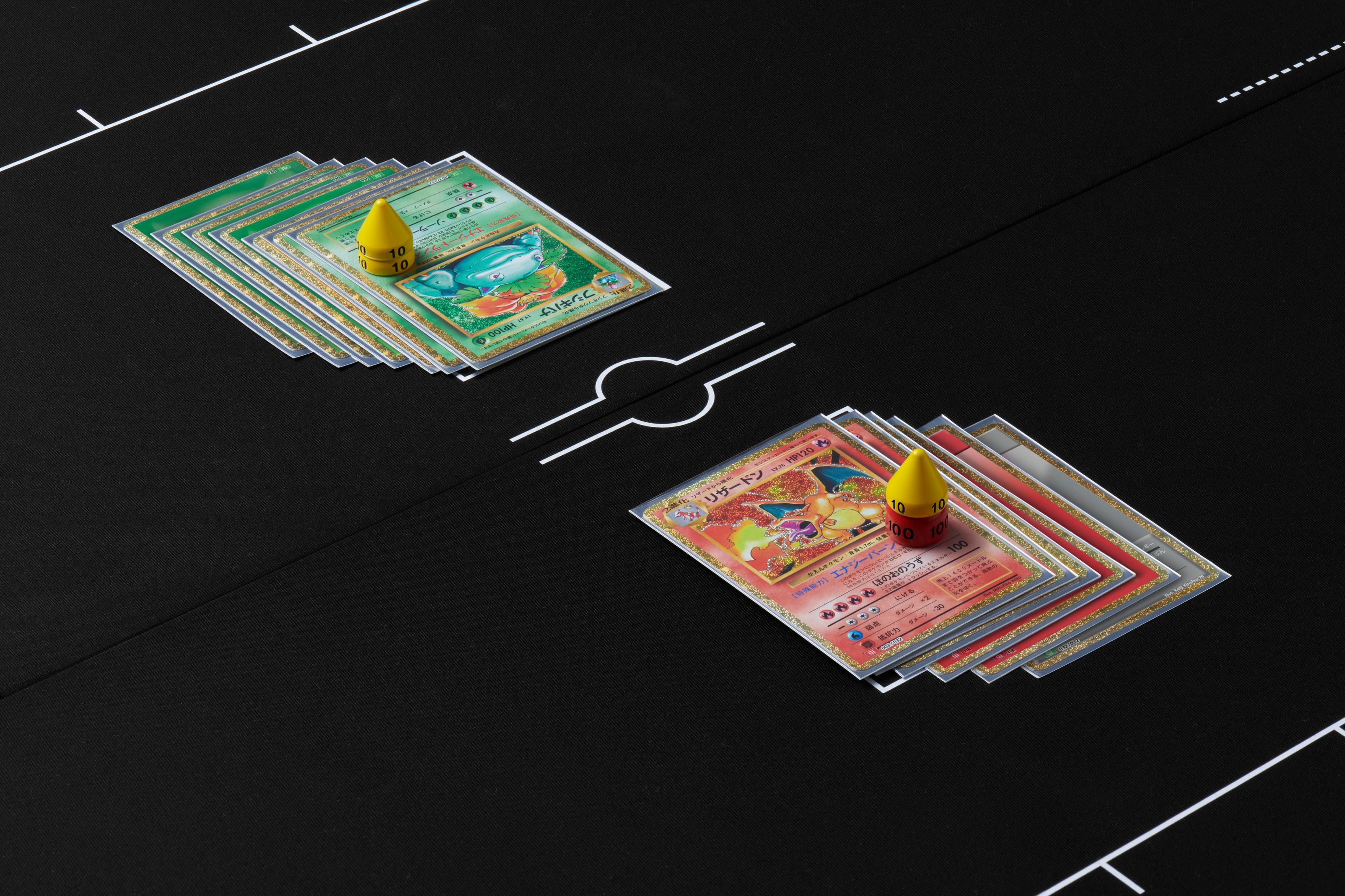 Des cartes Pokemon sont placées sur une surface sombre, avec deux pions jaunes.