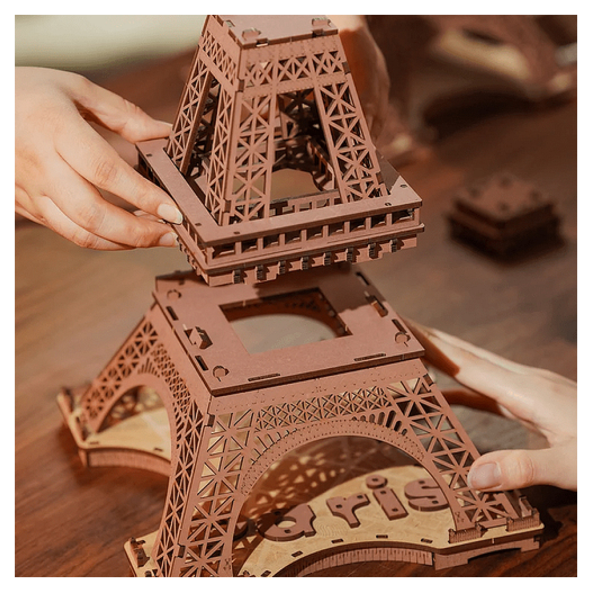 Dłonie składające drewniany model wieży Eiffla, pokazujące proces budowy.