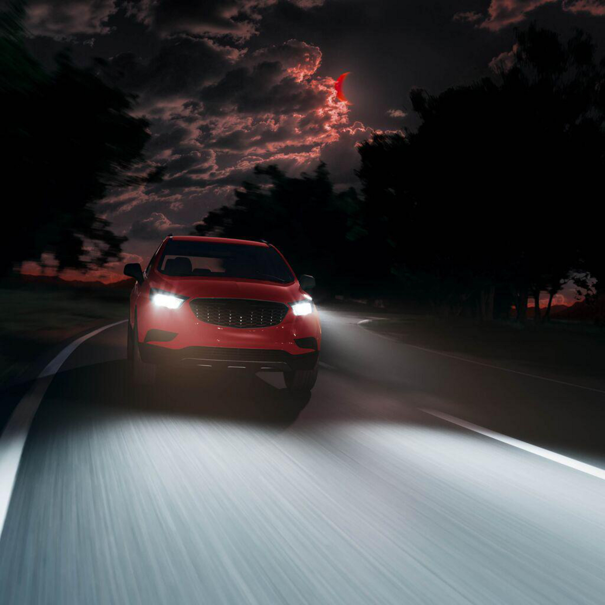 Rotes Auto fährt nachts auf einer Straße mit hellen Scheinwerfern.