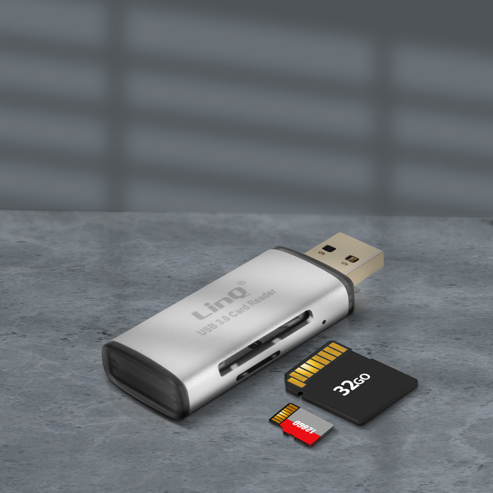 Un lettore di schede USB 3.0 argentato con schede SD e Micro SD su una superficie grigia strutturata.