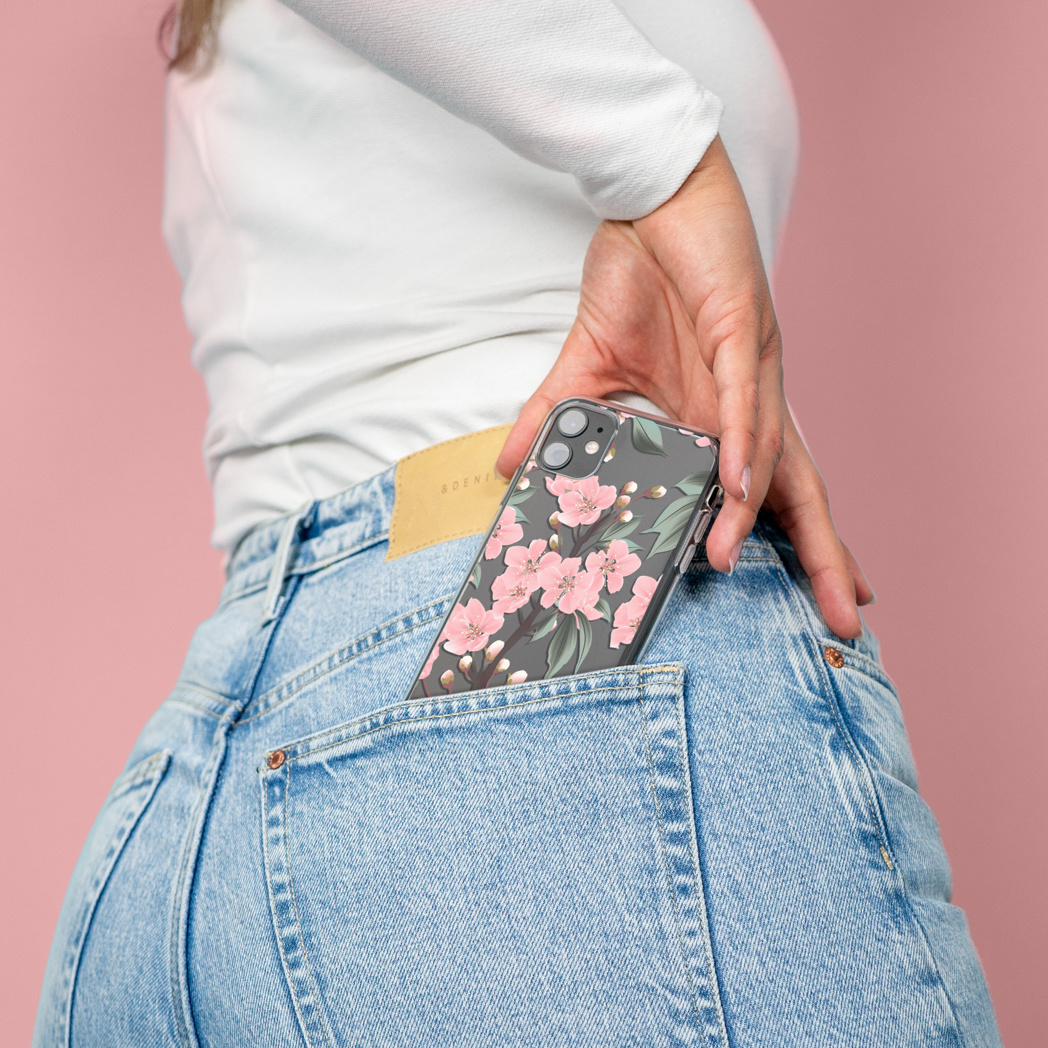 La main d'une femme mettant une coque de téléphone à fleurs dans une poche de jean.