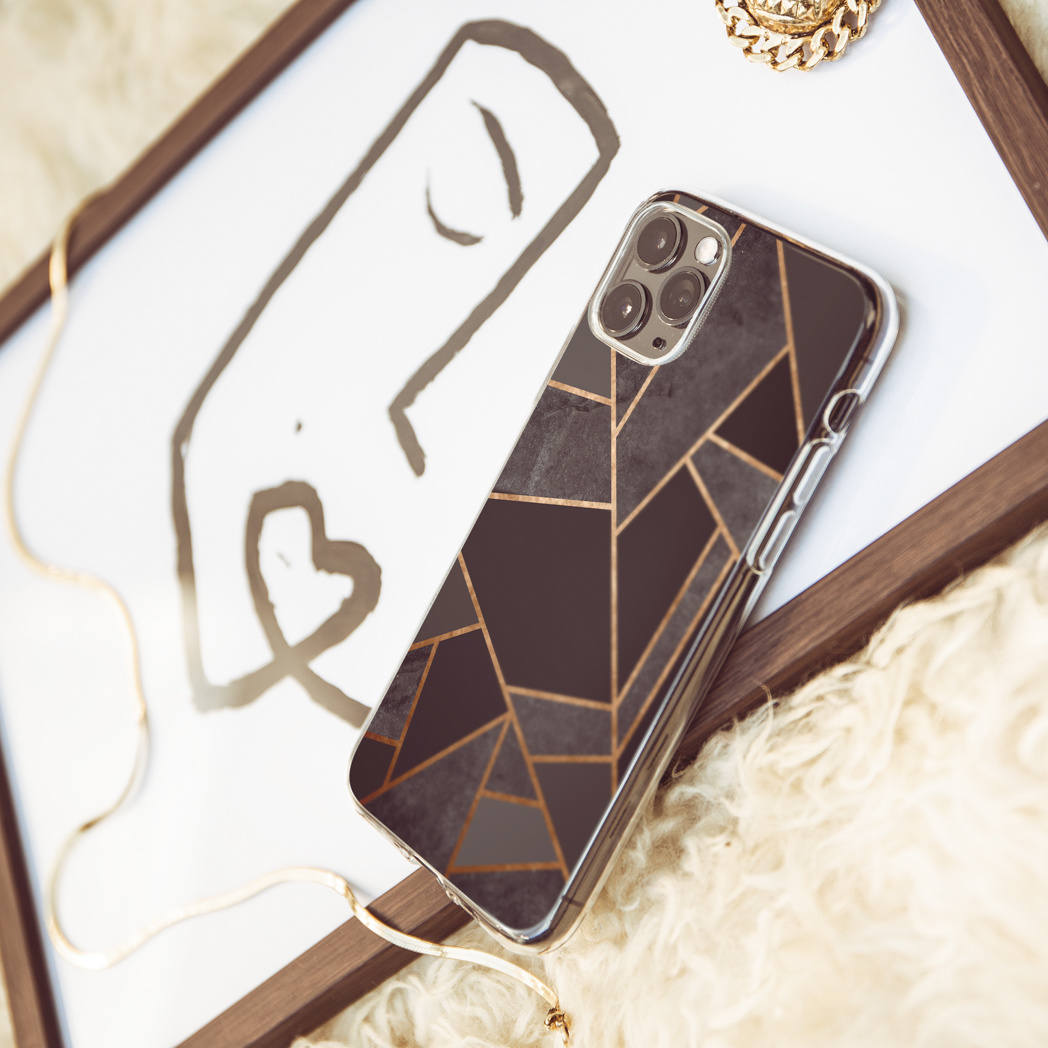 Telefoonhoesje met een zwart-gouden geometrisch ontwerp met een ketting en sieraden op een witte achtergrond.