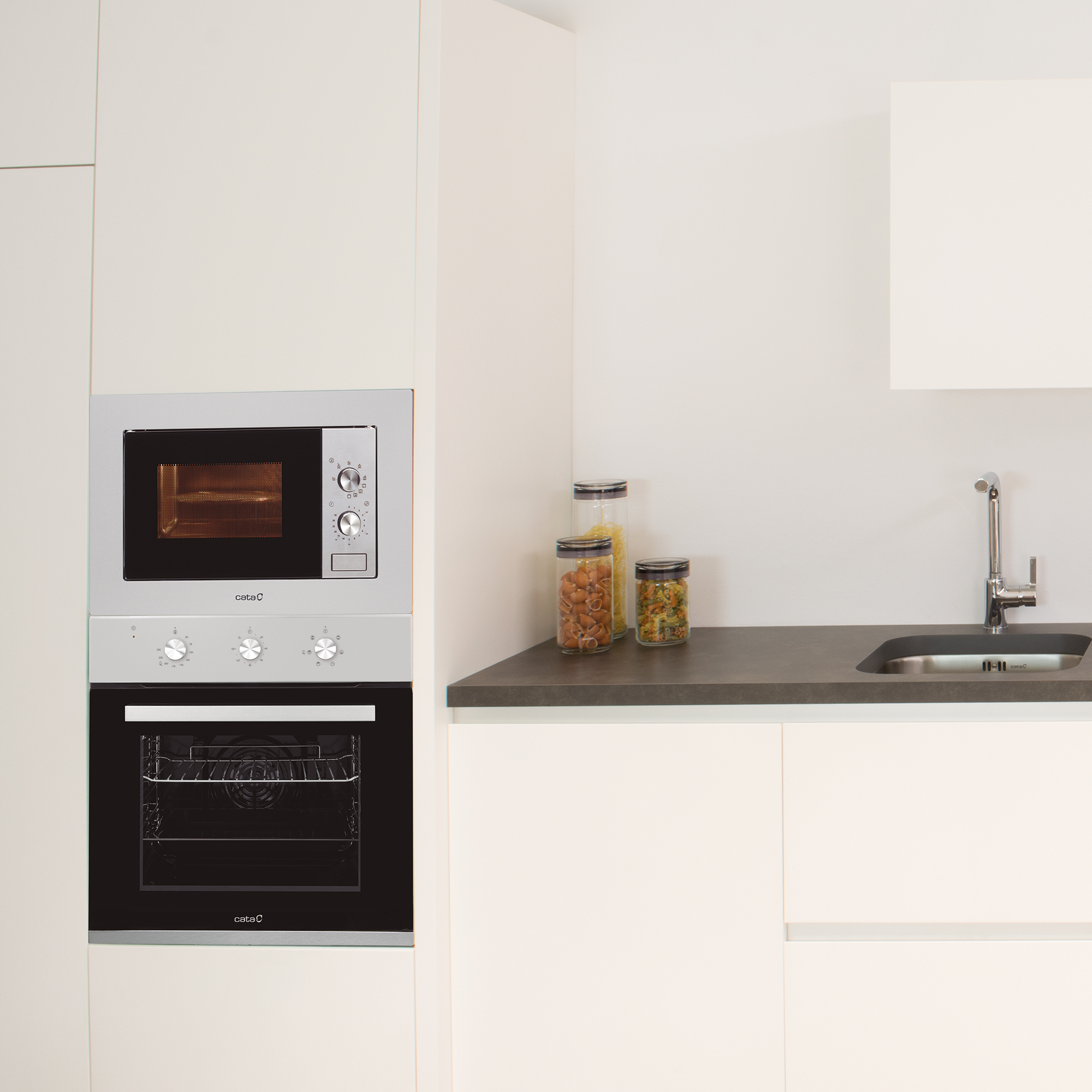 Microondas y horno empotrados. Gabinetes de cocina blancos. Frascos con comida en la encimera.