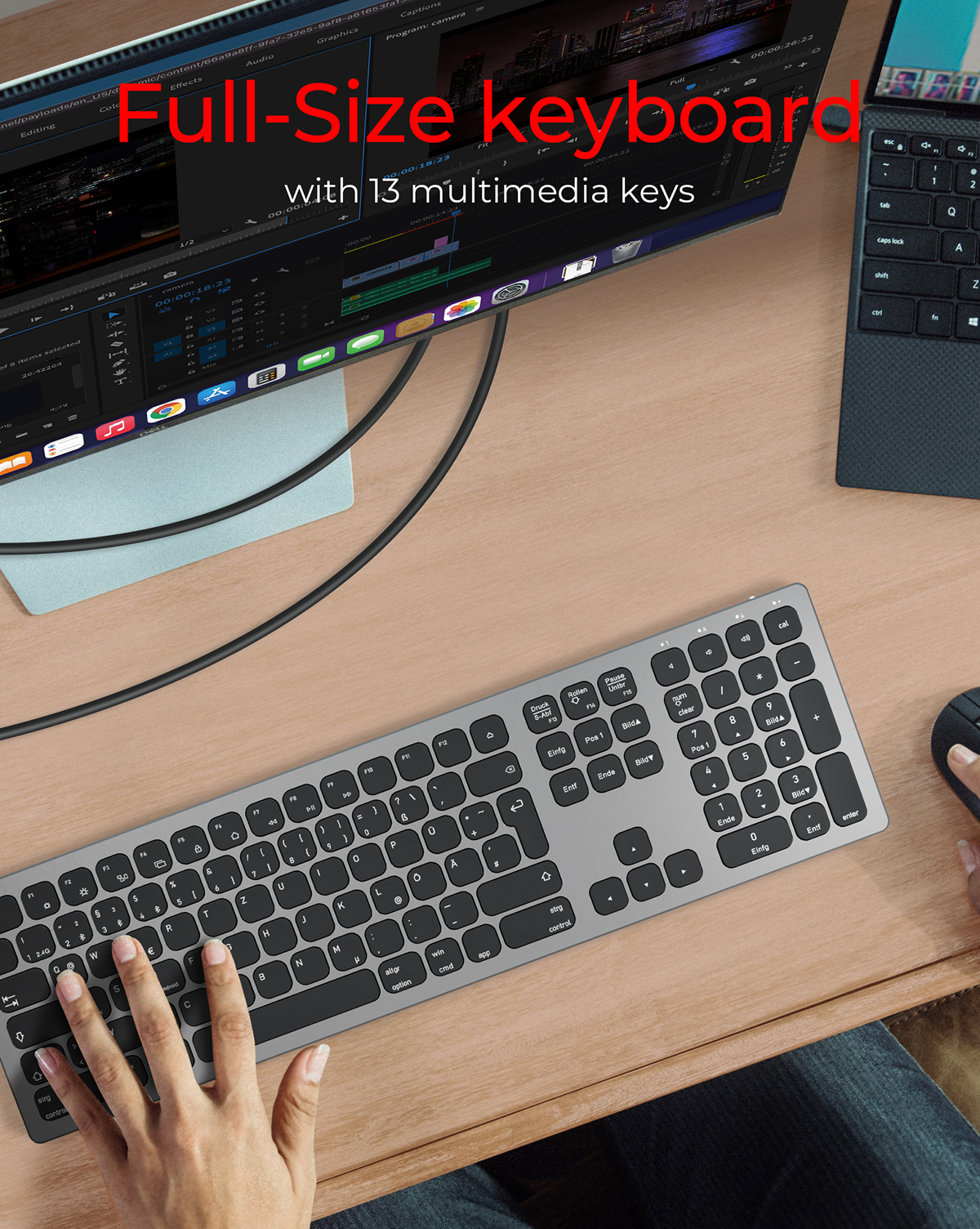 Pełnowymiarowa klawiatura z klawiszami multimedialnymi. Jest srebrna i ma czarne klawisze. Monitor w tle.