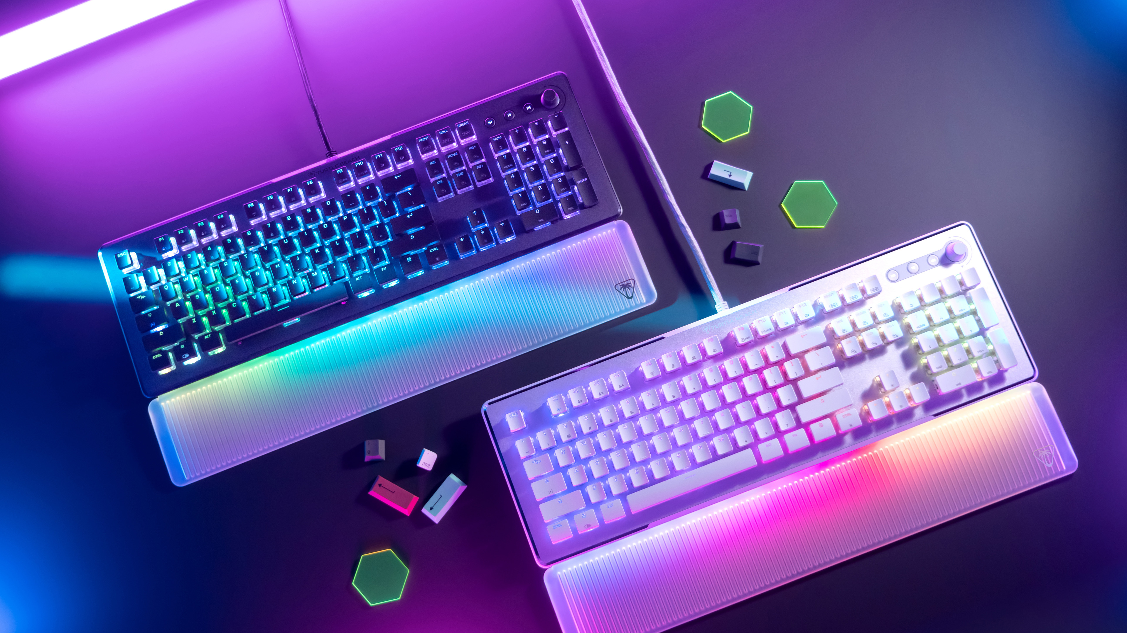 Dwie klawiatury dla graczy z kolorowym podświetleniem. Klawiatury leżą na ciemnej powierzchni z sześciokątnymi kształtami.