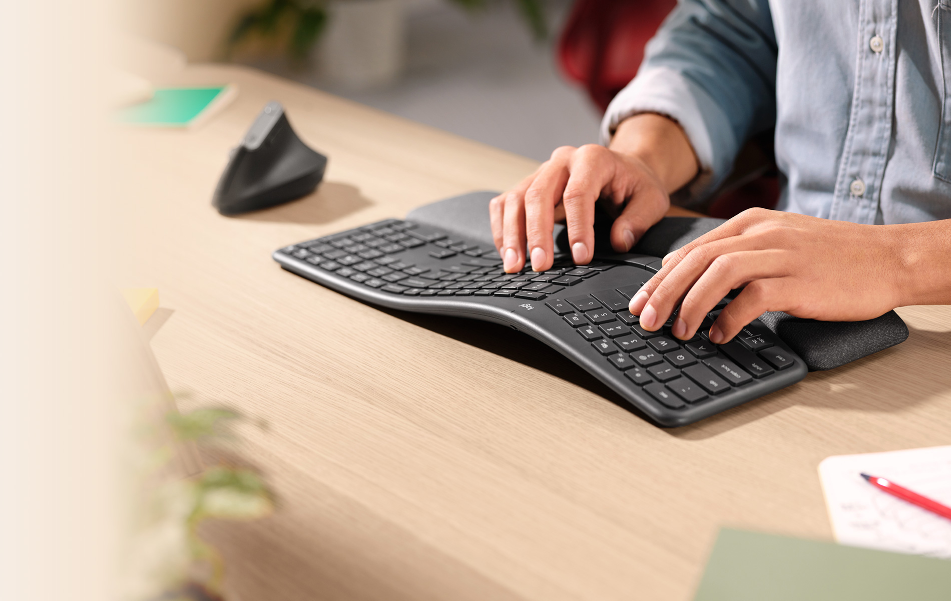 Persona che digita su una tastiera ergonomica curva con poggiapolsi su una scrivania.