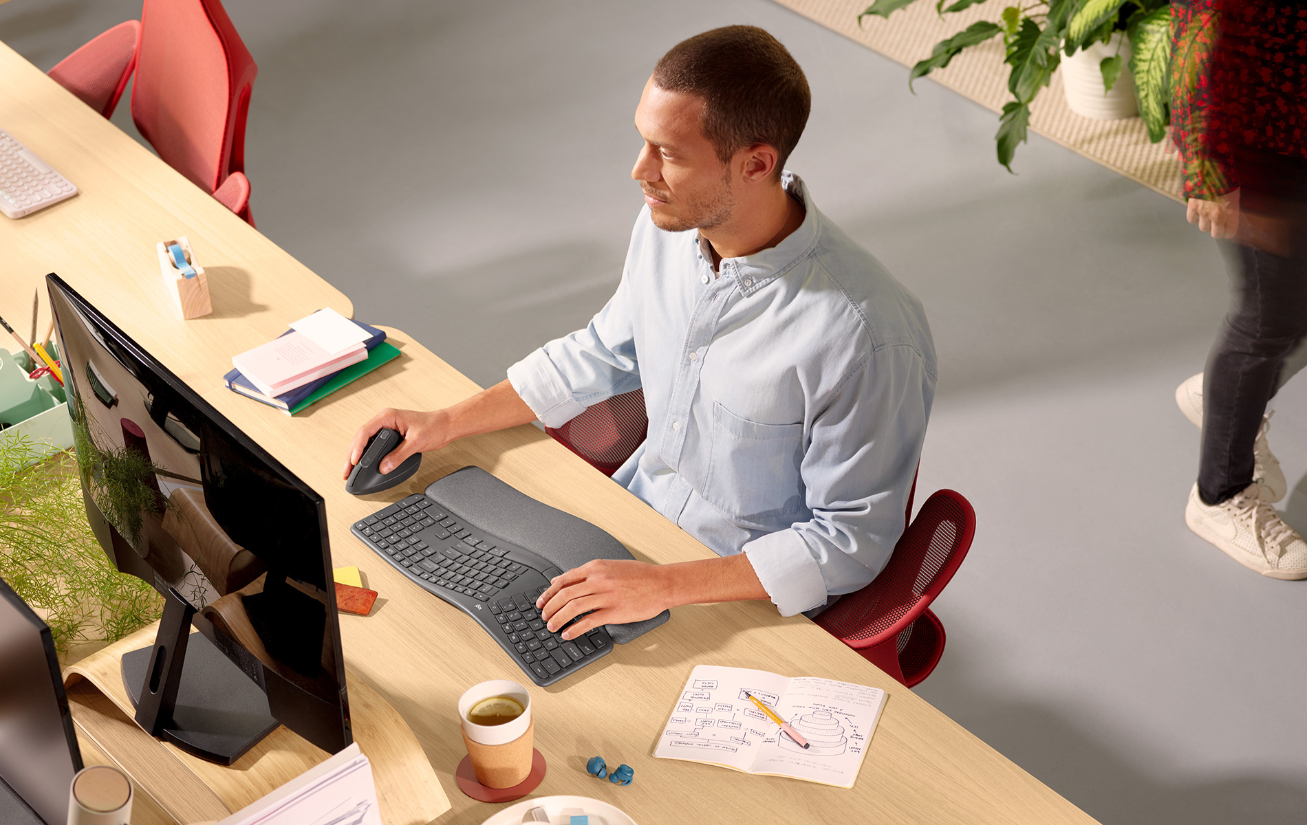 Uomo usa computer con tastiera e mouse curvi su scrivania in un ambiente ufficio.