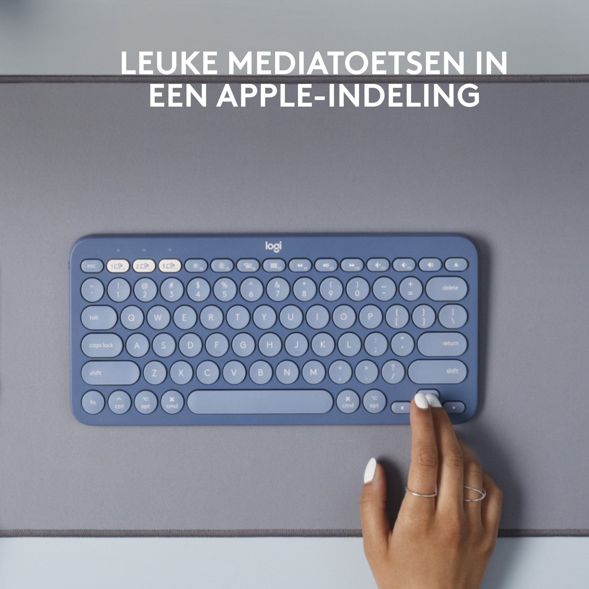Tastiera blu su tappetino grigio. Una mano usa il mouse. Testo sopra: "Tasti multimediali cool in un layout Apple".