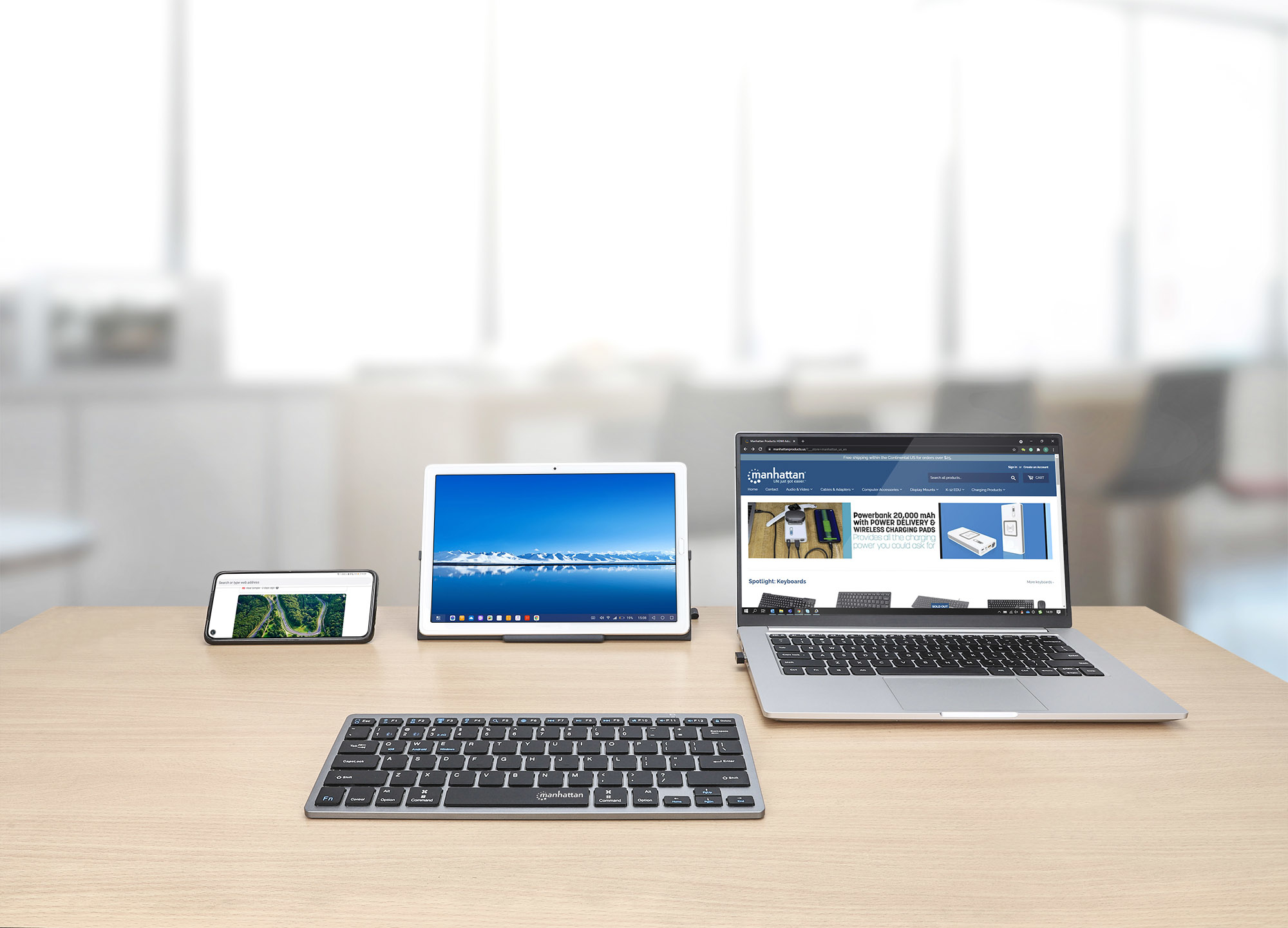 Urządzenia na biurku: telefon, tablet, laptop, klawiatura. Drewniana powierzchnia.